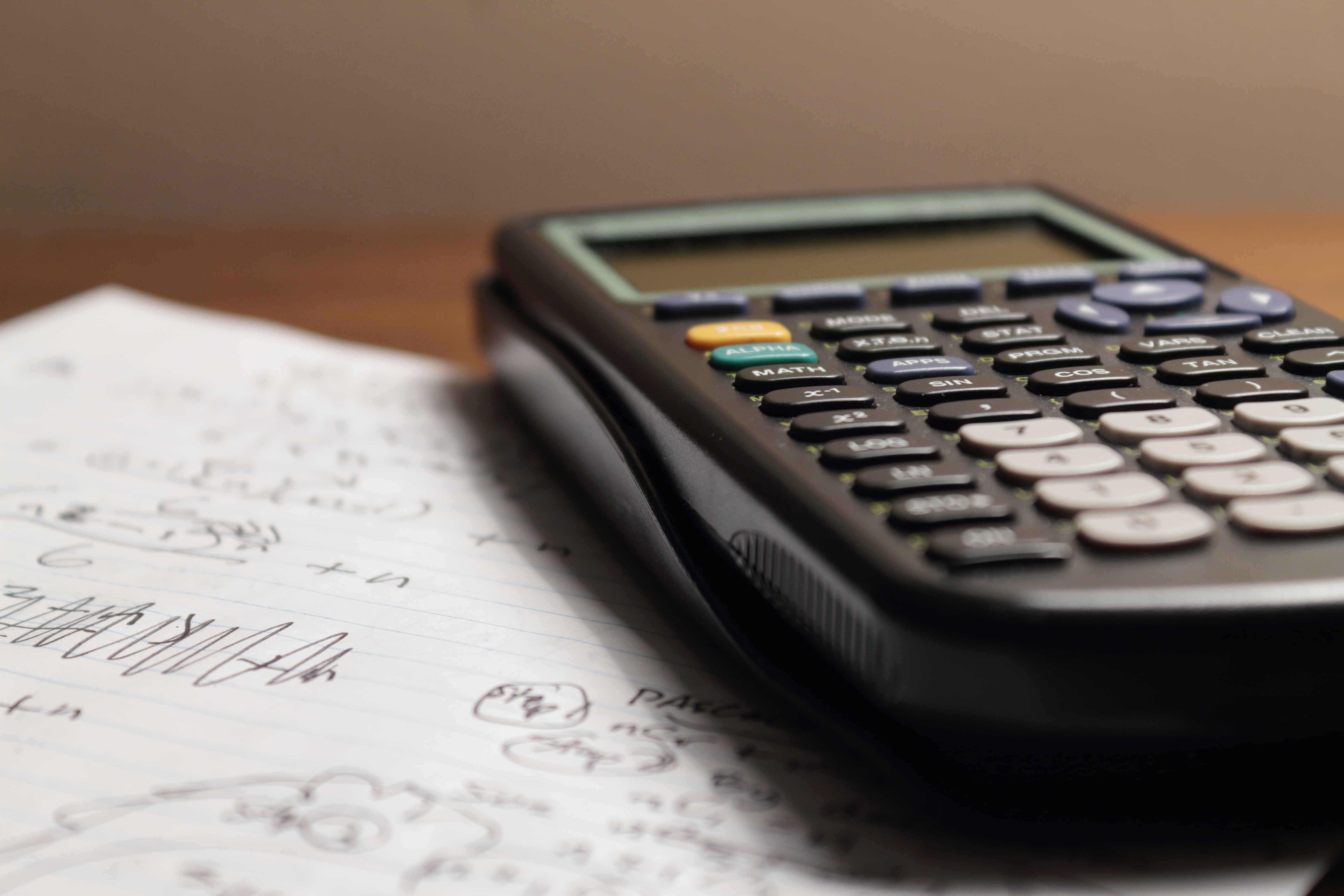 A graphing calculator sits atop a table beside a stack of papers