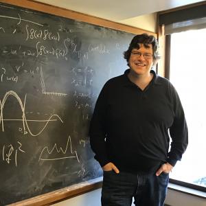 Rick stands in front of a chalkboard covered in math drawings