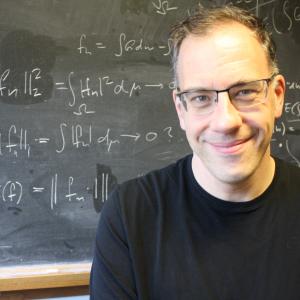Tilmann stands in front of a chalkboard with math drawn out
